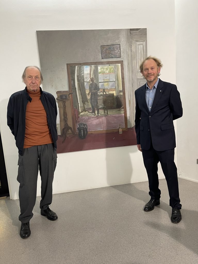 Ernst Hübner und James Lloyd (rechts) in der Frankfurter Galerie Hübner & Hübner vor dem zentralen Interieur der Ausstellung „Two Decades“. Das Spiegelbild zeigt den Maler in seinem Londoner Atelier, wo auch die Porträts der Galeristen entstanden. Foto: Edda Rössler